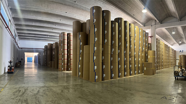 Massive production capacity demonstrated by warehouse storing numerous capacitor grade paper rolls.
