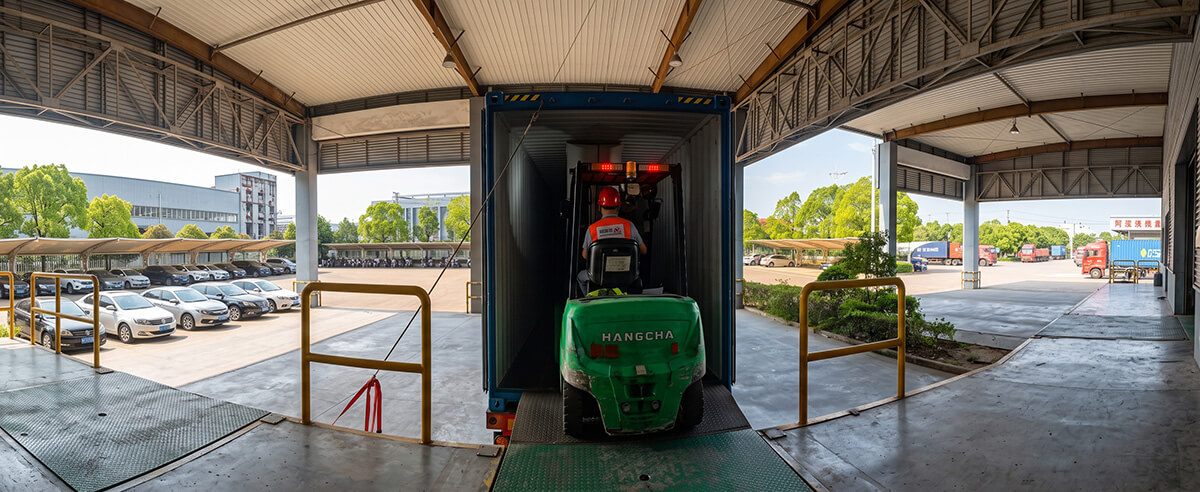 Forklift loading export pallets of baking paper sheets into shipping container at factory dock