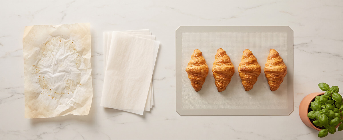Reusable silicone baking mat with croissants next to used parchment paper showing eco-friendly baking choice