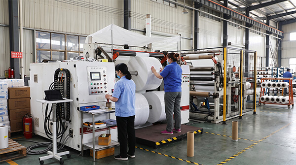 Factory technician operating a slitting machine for custom OEM electrolytic capacitor paper rolls.