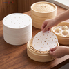 Placing precut round parchment steamer liner into bamboo steamer with steamed baozi on the side